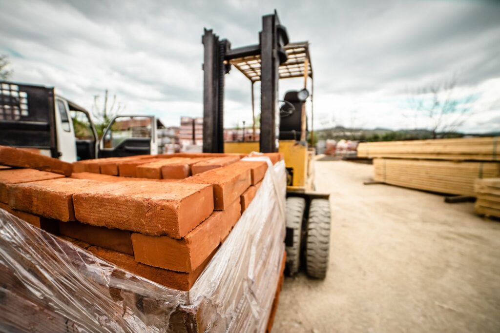 Forklift transporting a pallet of red bricks at an outdoor construction supply yard